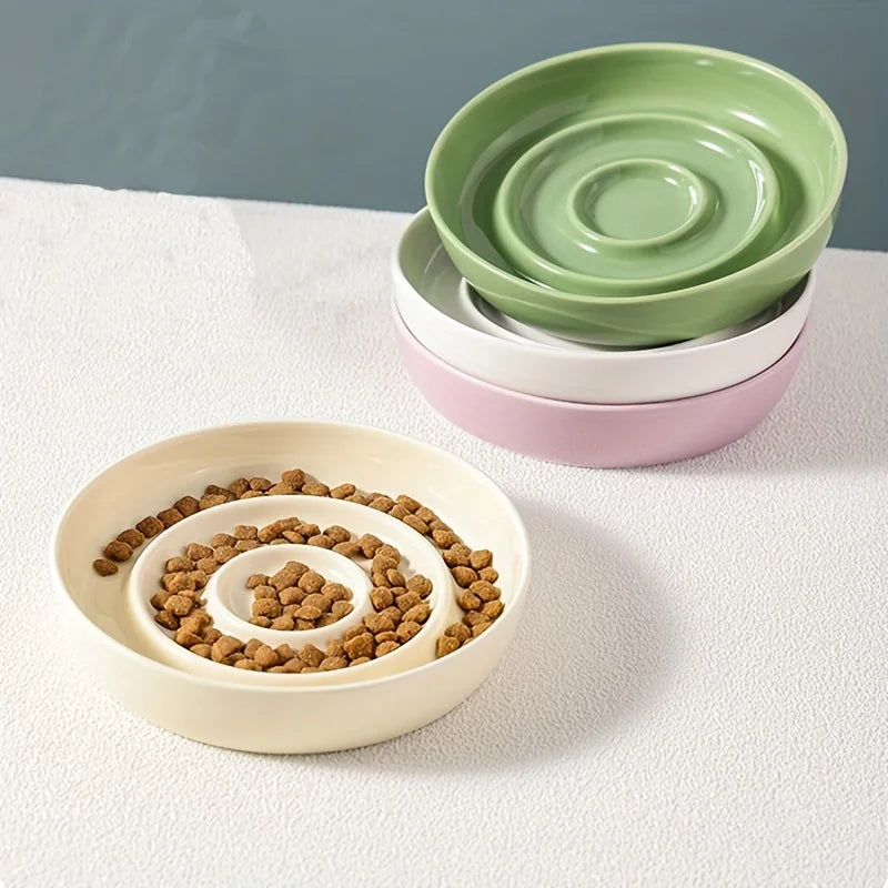 Gamelle anti-glouton en céramique beige avec croquettes pour chien, collier vert en arrière-plan.